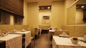Un restaurant avec des banquettes et des tables, chacune agrémentée d’une nappe blanche et de couverts en argent.