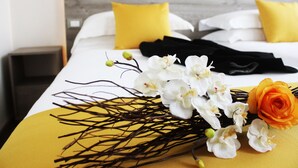 Un lit bien fait, avec une literie blanche et jaune, une robe noire, des orchidées blanches et une rose orange.