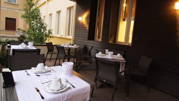 Un espace de restauration en plein air avec des tables pour deux personnes, des chaises et une nappe blanche.