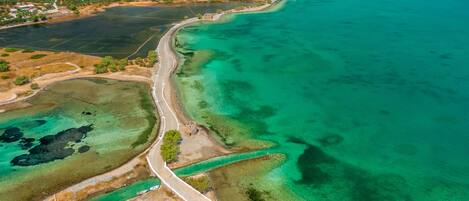 Une vue aérienne d’une ville côtière, avec une route sinueuse longeant la côte, des eaux d’un bleu limpide et un mélange de paysages résidentiels et naturels.