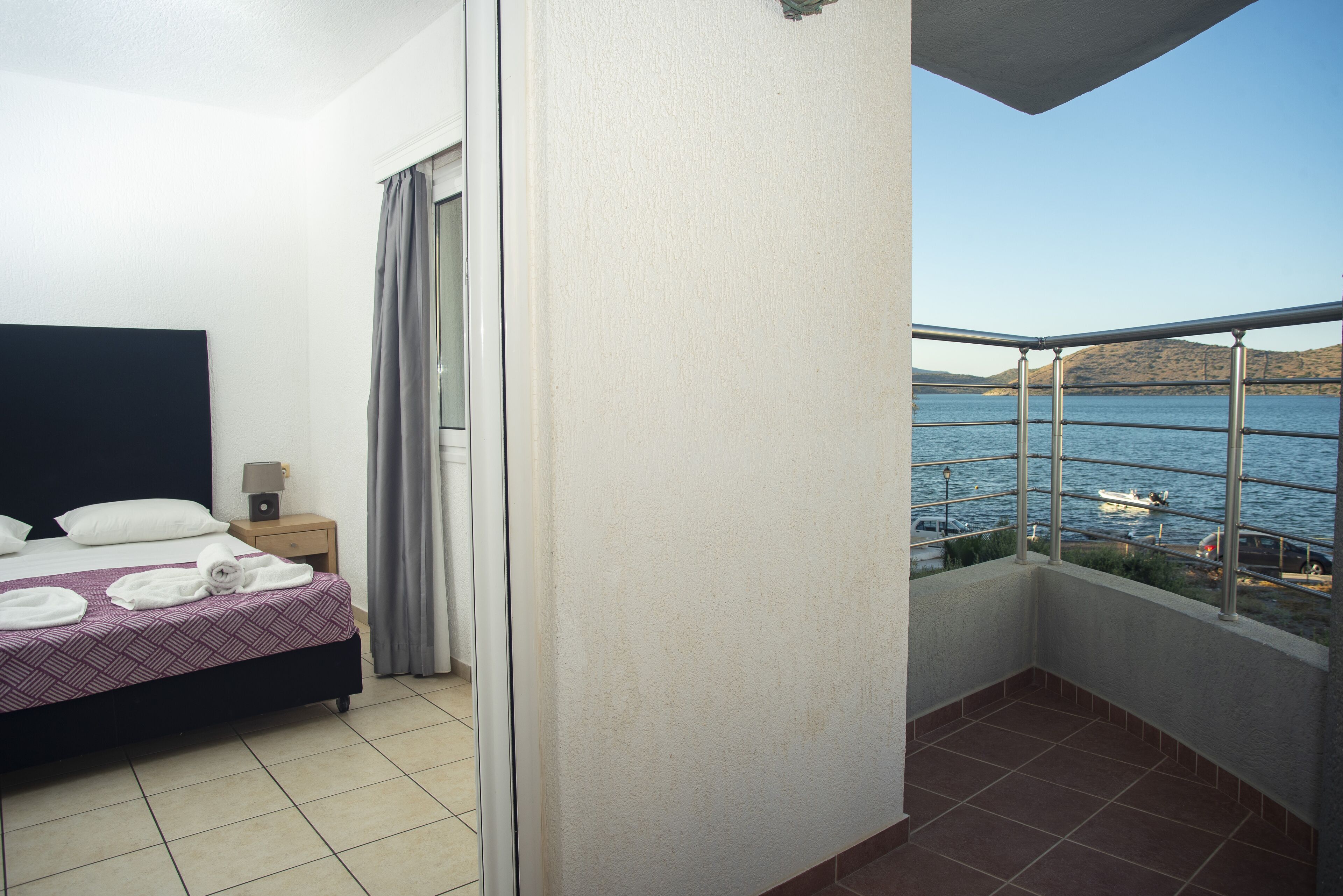 Et hotelværelse med en seng, et natbord, et vindue med havudsigt og en balkon med gelænder.