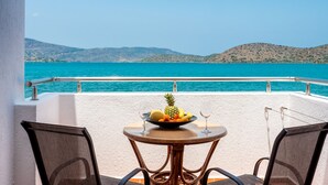 A balcony with a table set for two, overlooking a turquoise sea and distant hills. - Elounda Alikes Suites & Studios (Agios Nikolaos)