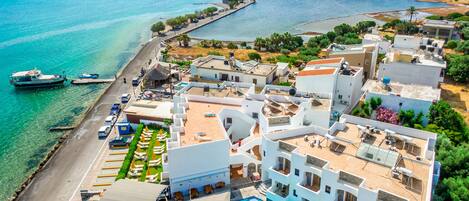 A coastal hotel with a swimming pool, multiple balconies, and a view of the sea.