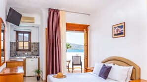 A hotel room with a bed, a desk with a sink, a television, and a view of the sea. - Elounda Alikes Suites & Studios (Agios Nikolaos)