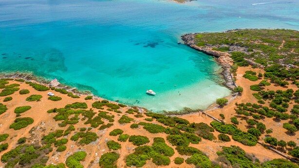 An aerial view of a coastal area with clear turquoise waters, a sandy beach, and green vegetation. - Elounda Alikes Suites & Studios (Agios Nikolaos)