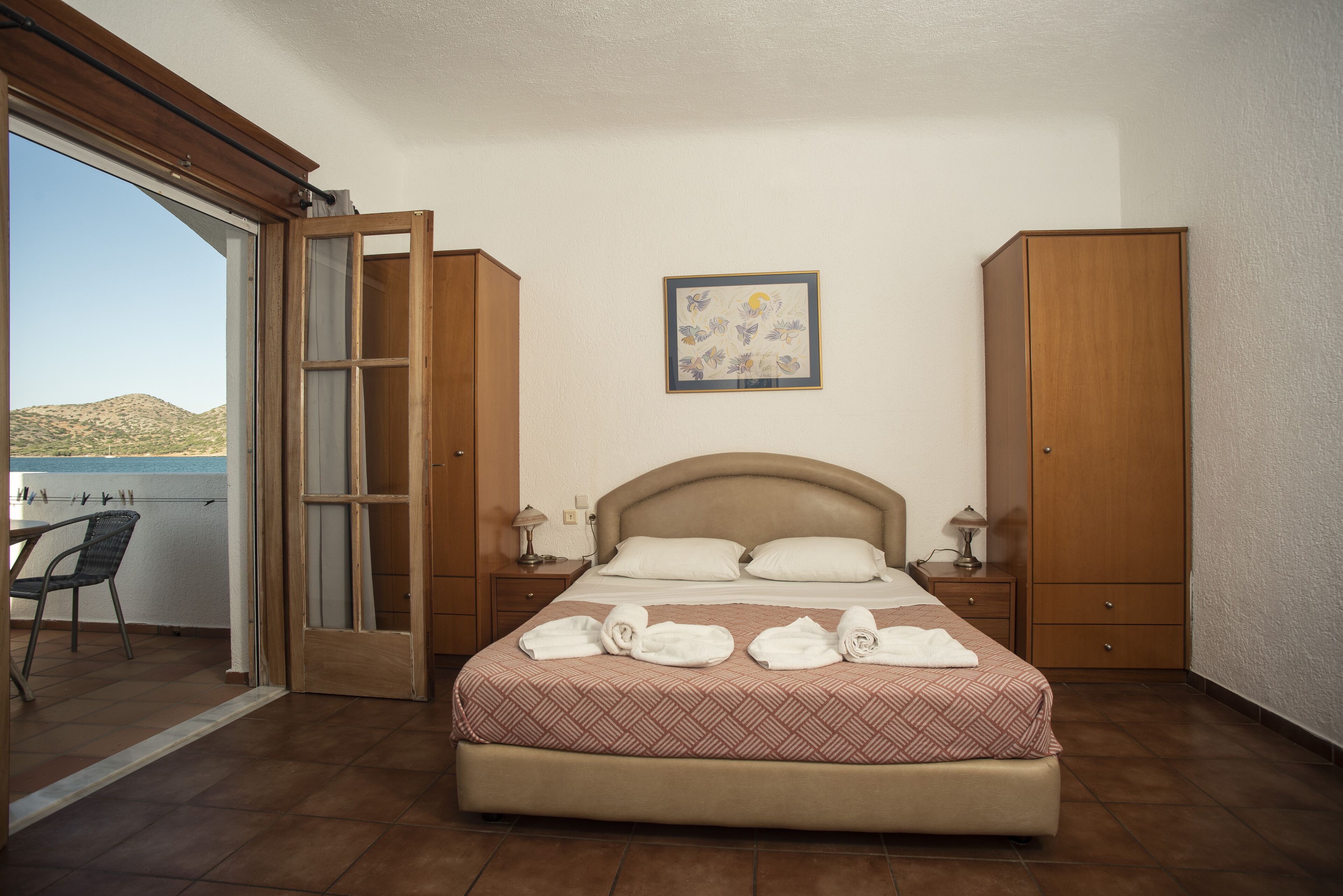 A bedroom with a bed, a nightstand, a chair, a wardrobe, and a sliding glass door leading to a balcony.