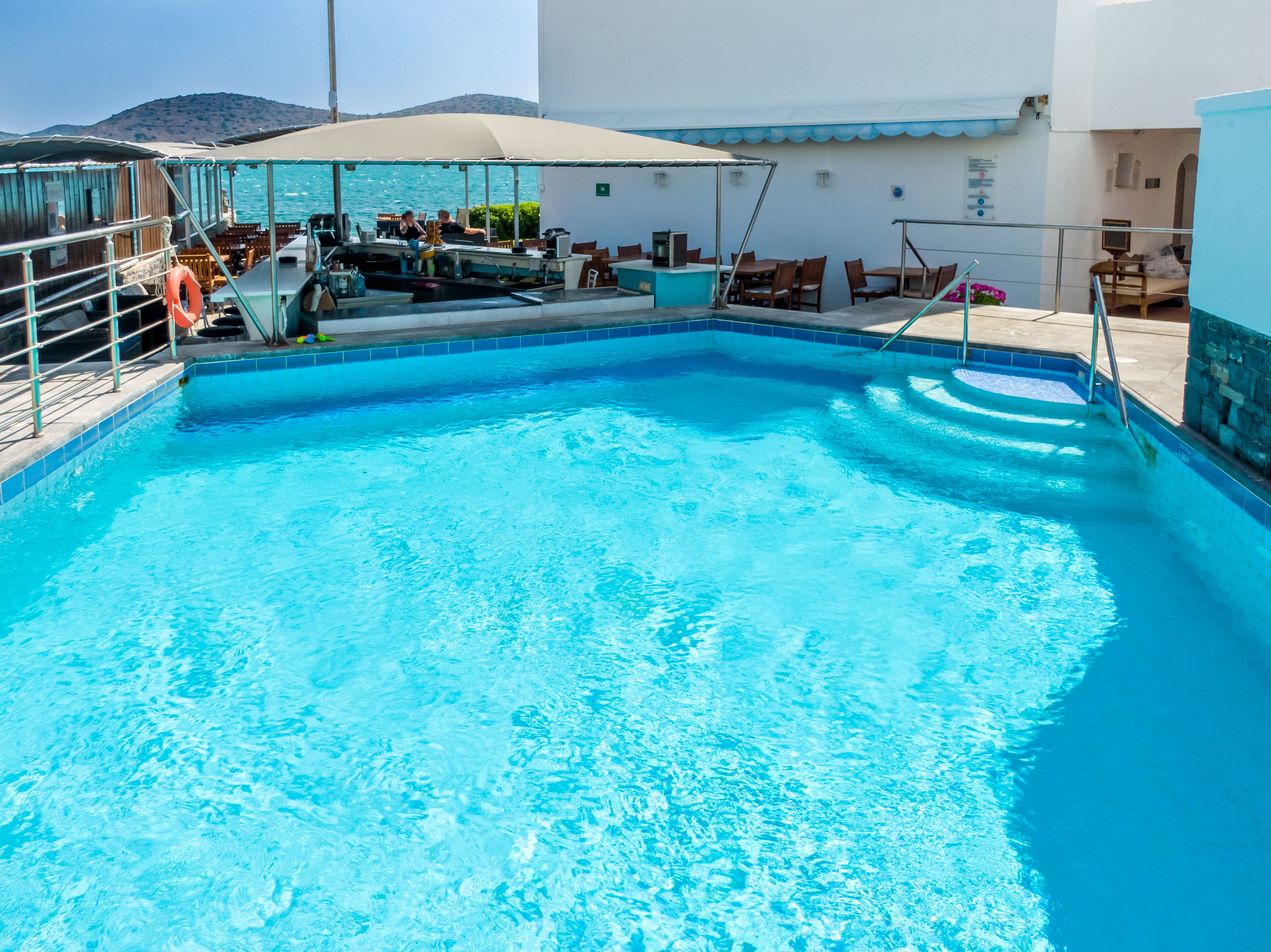 Una piscina con sombrilla, sillas de descanso y vistas al mar.