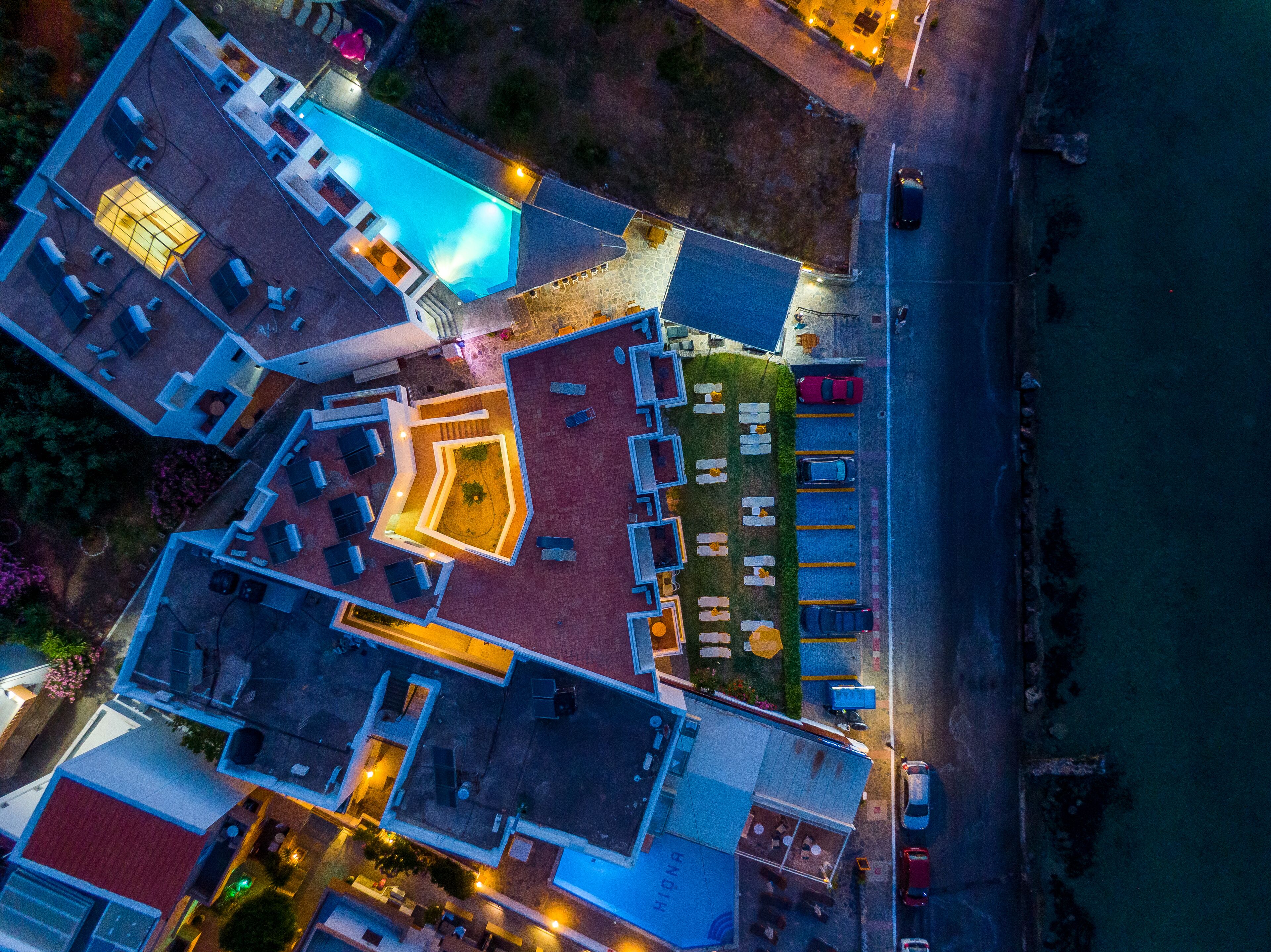 An aerial view of a hotel with a swimming pool, outdoor seating, and a parking lot.