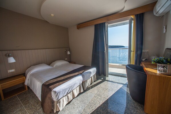 A hotel room with a bed, bedside table, lamp, and a view of the sea. - El Greco Hotel (Agios Nikolaos)