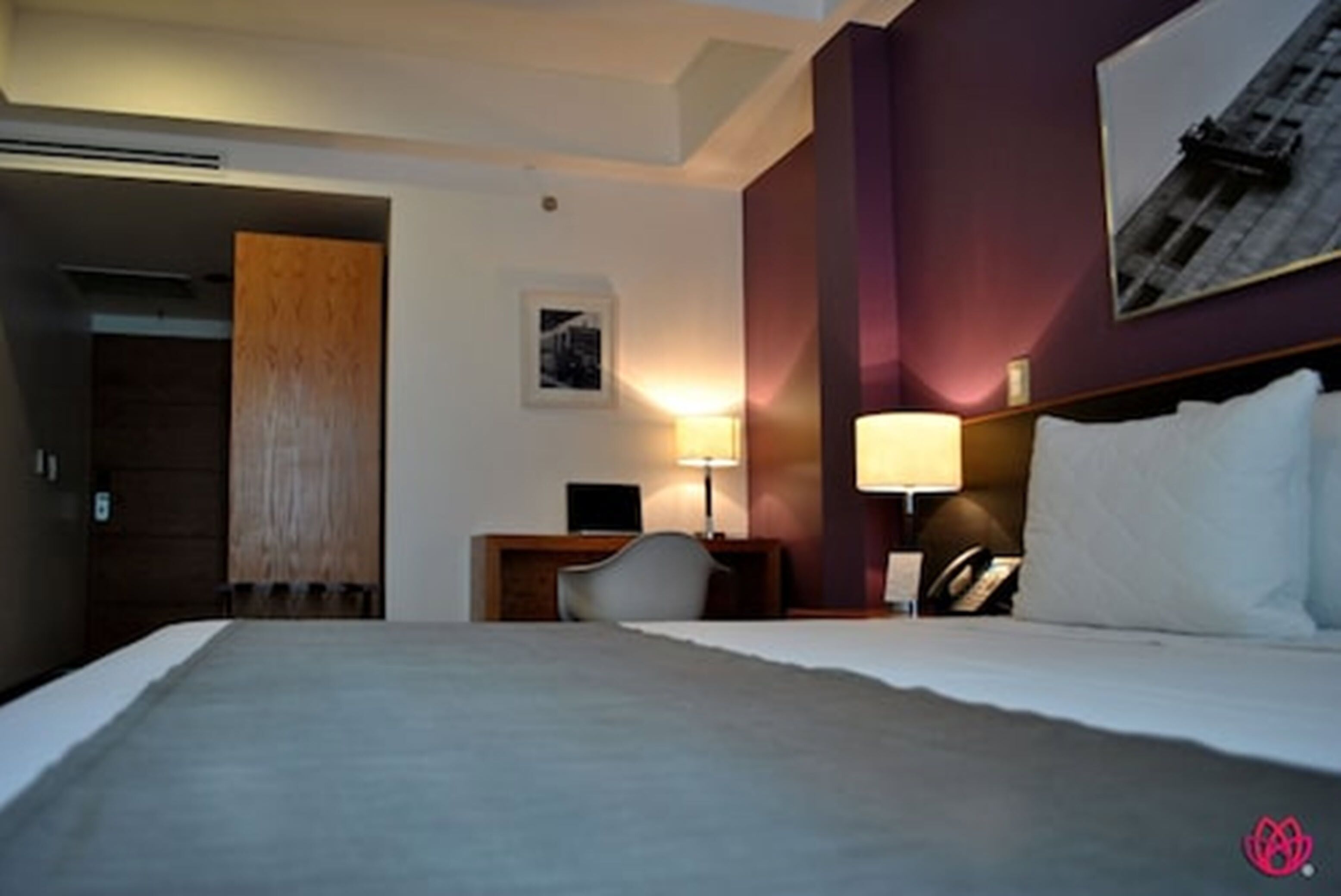 A hotel room with a large bed, a desk with a lamp, a chair, and a wall-mounted phone.