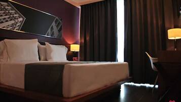 Una camera d'albergo con un letto grande, un comodino con una lampada, una sedia e vista su un edificio dalla finestra.