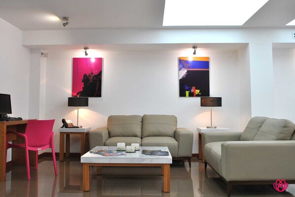 Un salon moderne comprenant un canapé, des fauteuils, une table basse et deux lampes. Deux œuvres d’art sont accrochées au mur, et un téléviseur à écran plat est posé sur un meuble.