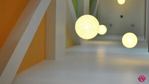 A modern interior with a geometric design, featuring a white wall, a green accent wall, and a large white door. There are three spherical light fixtures on the ceiling. - Hotel y Tú (Guadalajara)