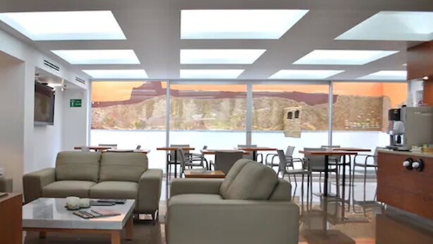 A modern lounge area with sofas, tables, and a view of a mountainous landscape through large windows. - Hotel y Tú (Guadalajara)