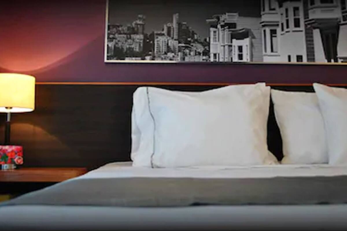 A hotel room with a bed, a nightstand with a lamp, and a cityscape picture on the wall.