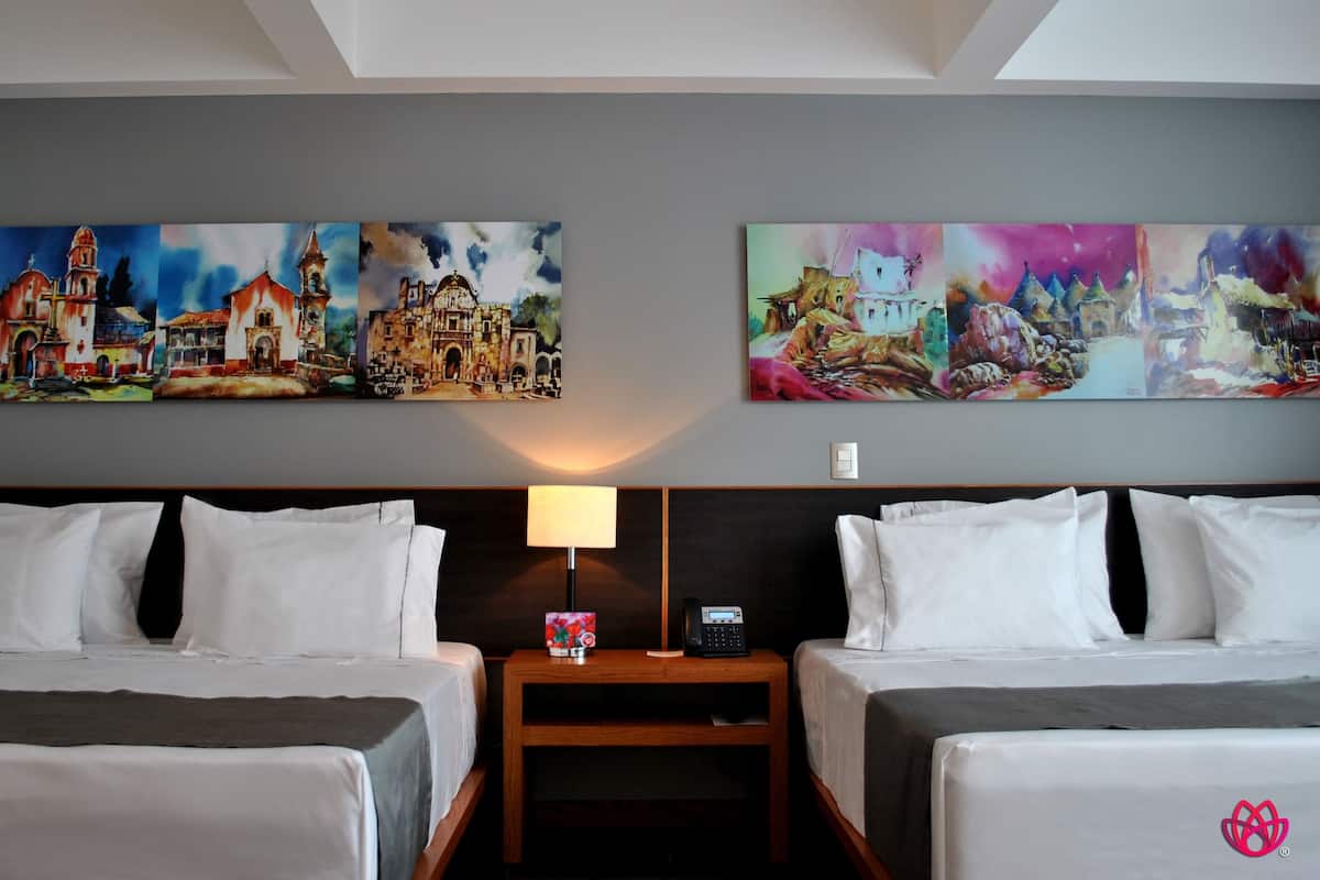 A hotel room with two beds, a nightstand with a lamp and phone, and two large paintings on the wall.