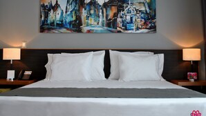 A hotel room with a large bed, white bedding, two bedside lamps, a telephone on the left nightstand, and a painting above the bed. - Hotel y Tú (Guadalajara)