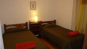 A small, dimly lit room with two single beds, a nightstand with a lamp, and a framed inspirational quote on the wall.