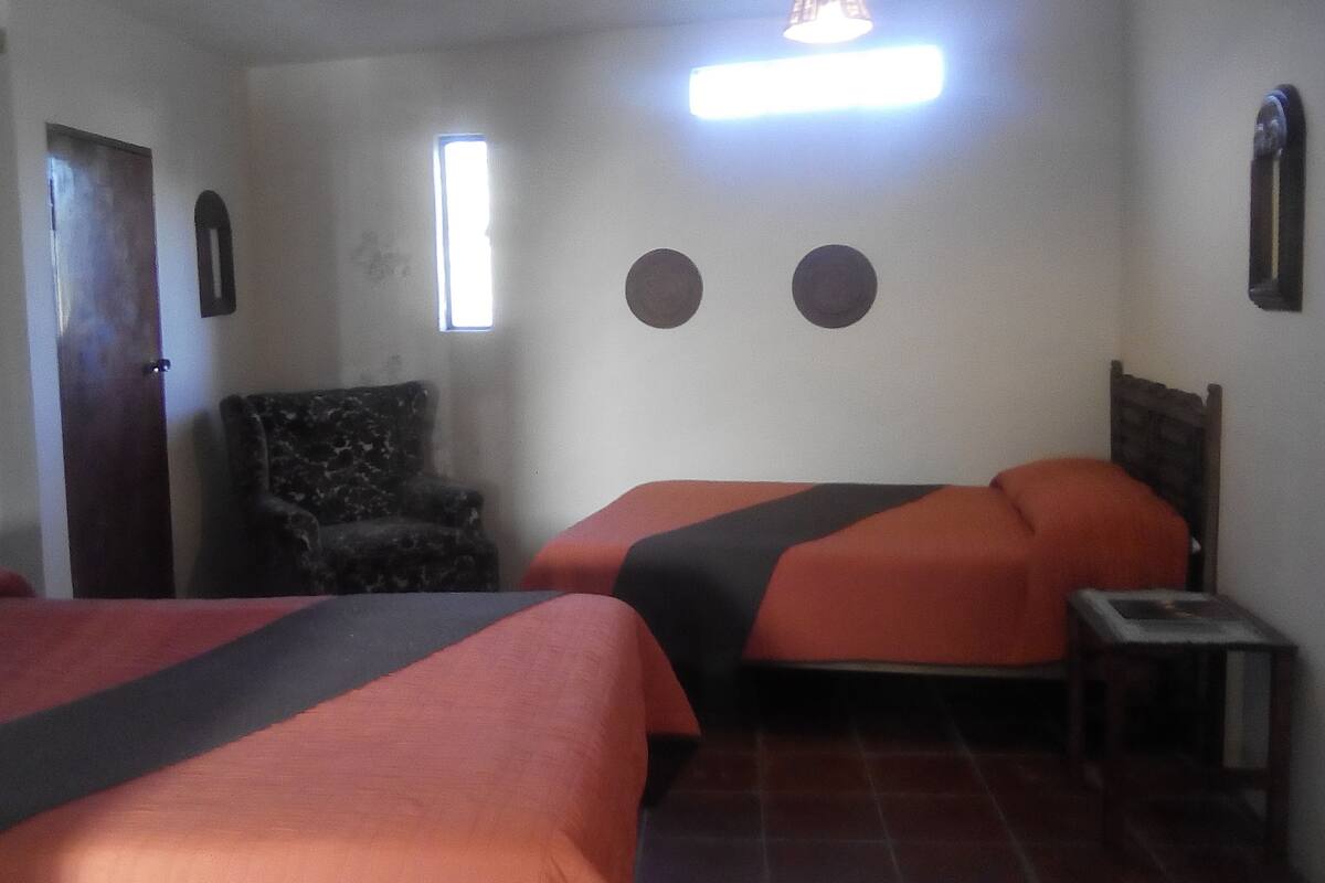Una habitación de hotel con dos camas, una silla, una mesita y un ventanal.