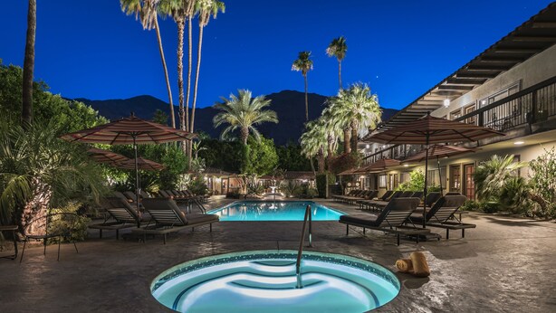 A pool area with lounge chairs and umbrellas, surrounded by palm trees and a mountain in the background.