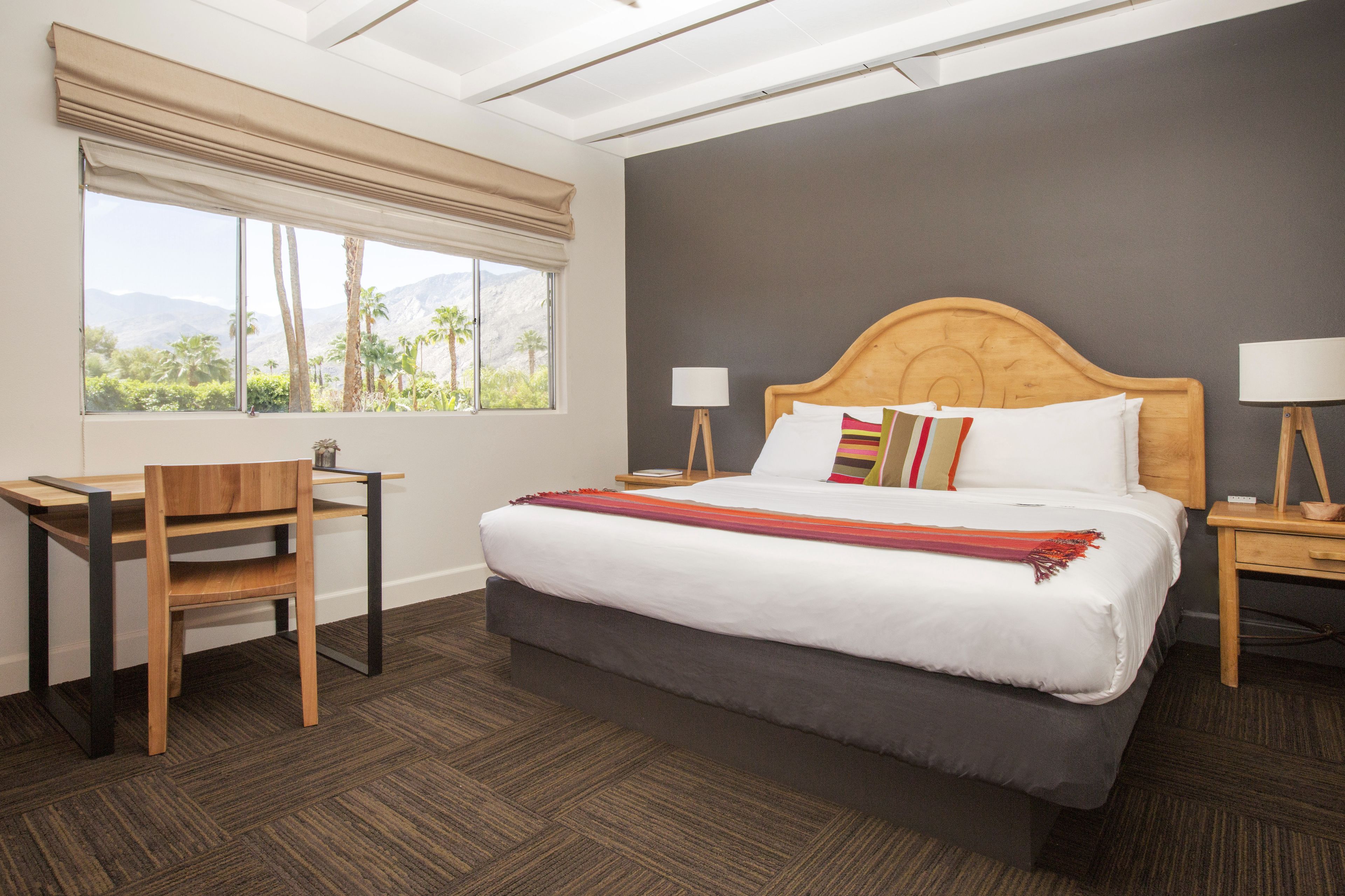 A hotel room with a large bed, a desk, and a window with a view of palm trees and mountains.