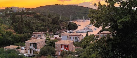Un pueblo costero con edificios de piedra, un puerto deportivo con barcos y una colina al fondo.