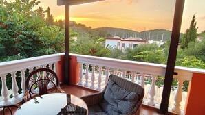 Ein Balkon mit Tisch und Stühlen, der einen schönen Ausblick auf Hügel und einen Yachthafen bietet.