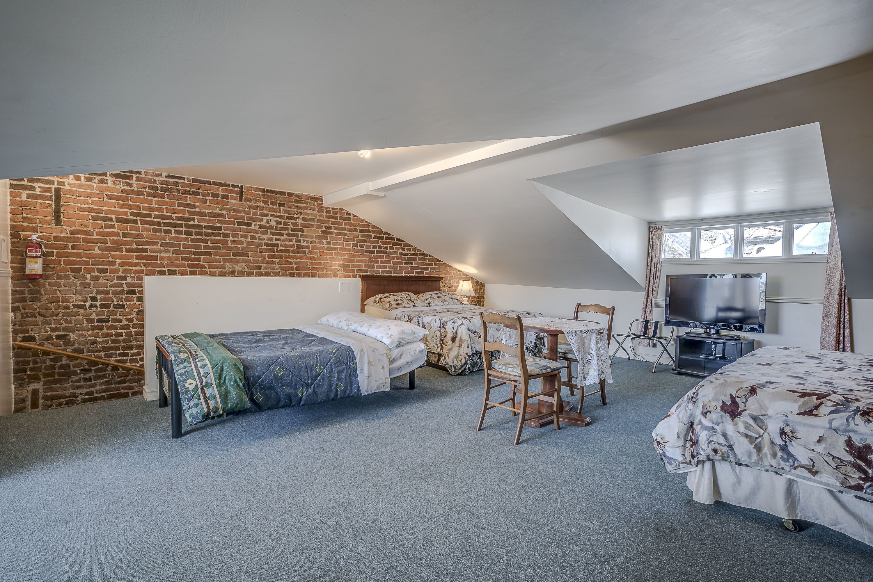 A bedroom with two beds, a small table, a TV, and a brick wall.