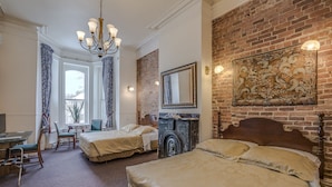 Habitación de hotel con dos camas, chimenea, candelabro, espejo grande y pared de ladrillo.