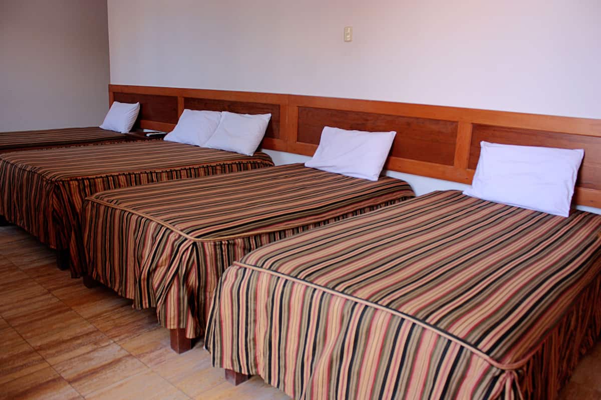 A hotel room with three single beds, each with a striped bedspread and white pillows.
