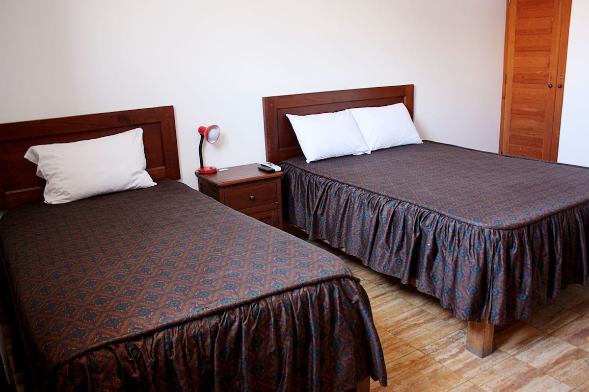 Two single beds with wooden headboards and matching pillows, a nightstand with a lamp, and a wooden door.