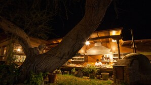 A rustic outdoor kitchen area with a chef preparing food, surrounded by potted plants and a large tree. - El Huarango Hotel (Ica)
