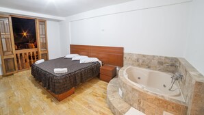 A bedroom with a bed, a wooden headboard, a built-in bathtub, and a wooden floor. - El Huarango Hotel (Ica)