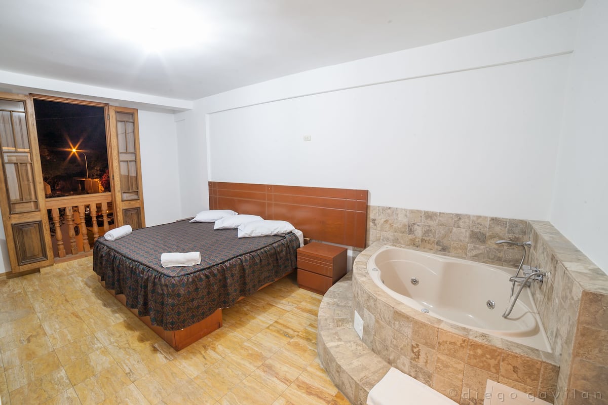 A bedroom with a bed, a wooden headboard, a built-in bathtub, and a wooden floor.