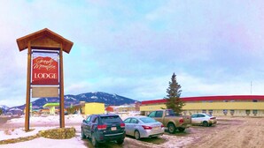 A lodge with a red and yellow building, a parking lot with several cars, and a mountainous backdrop. - Grande Mountain Lodge (Grande Cache)
