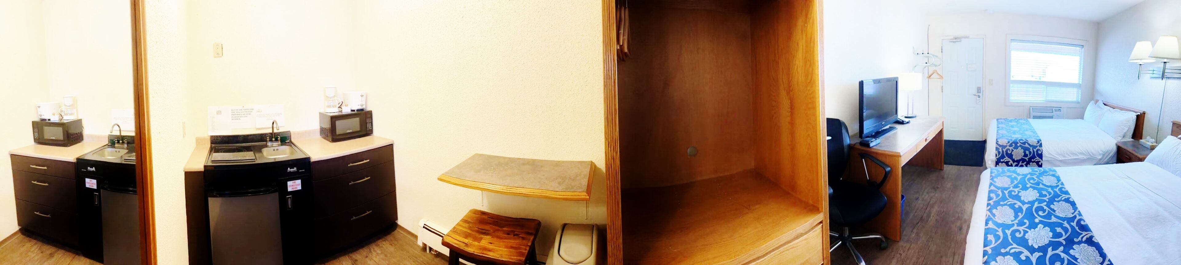A hotel room with a kitchenette, a bed, a desk, and a TV.