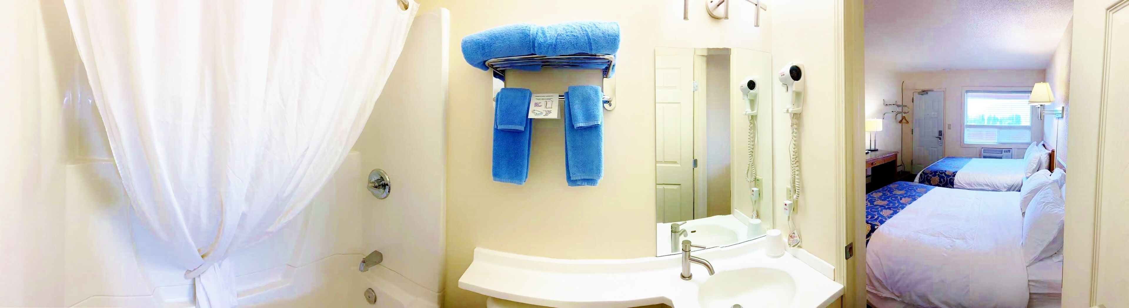 Une salle de bain avec une douche, un lavabo et un miroir. Deux serviettes sont accrochées au mur.