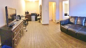 A living room with a leather sofa, a TV, a small kitchenette, and a radiator. - Grande Mountain Lodge (Grande Cache)