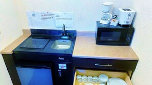 A compact kitchenette with a stove, sink, microwave, and a drawer with dishes. - Grande Mountain Lodge (Grande Cache)