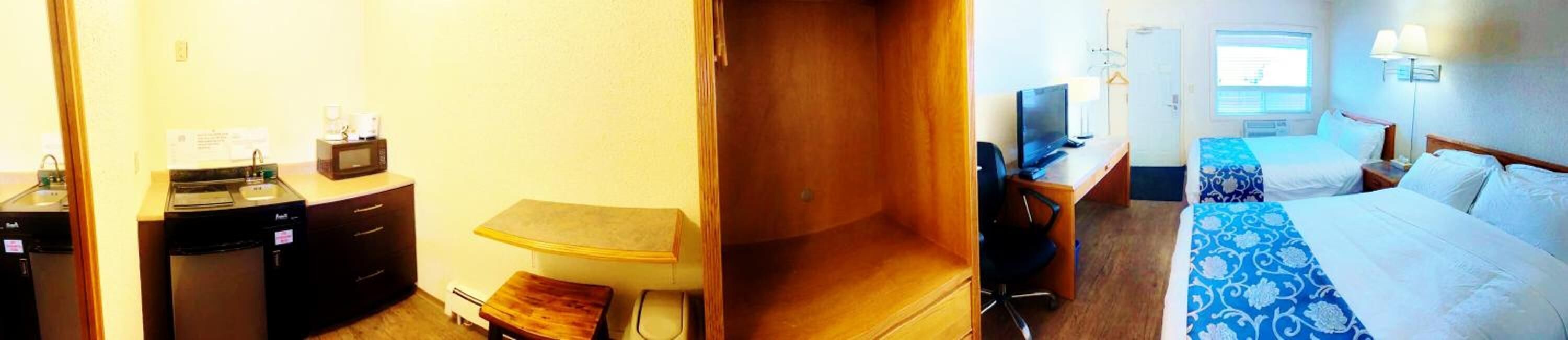 Et hotelværelse med tekøkken, et skrivebord med computer samt en seng med dynebetræk i blå og hvide mønstre, og et vindue med skodder.