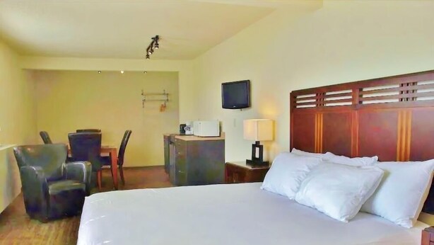 A hotel room with a large bed, a desk with a chair, a television, and a lamp. - Grande Mountain Lodge (Grande Cache)
