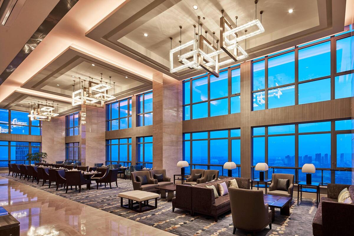 A spacious lobby with large windows, modern chandeliers, and comfortable seating areas.