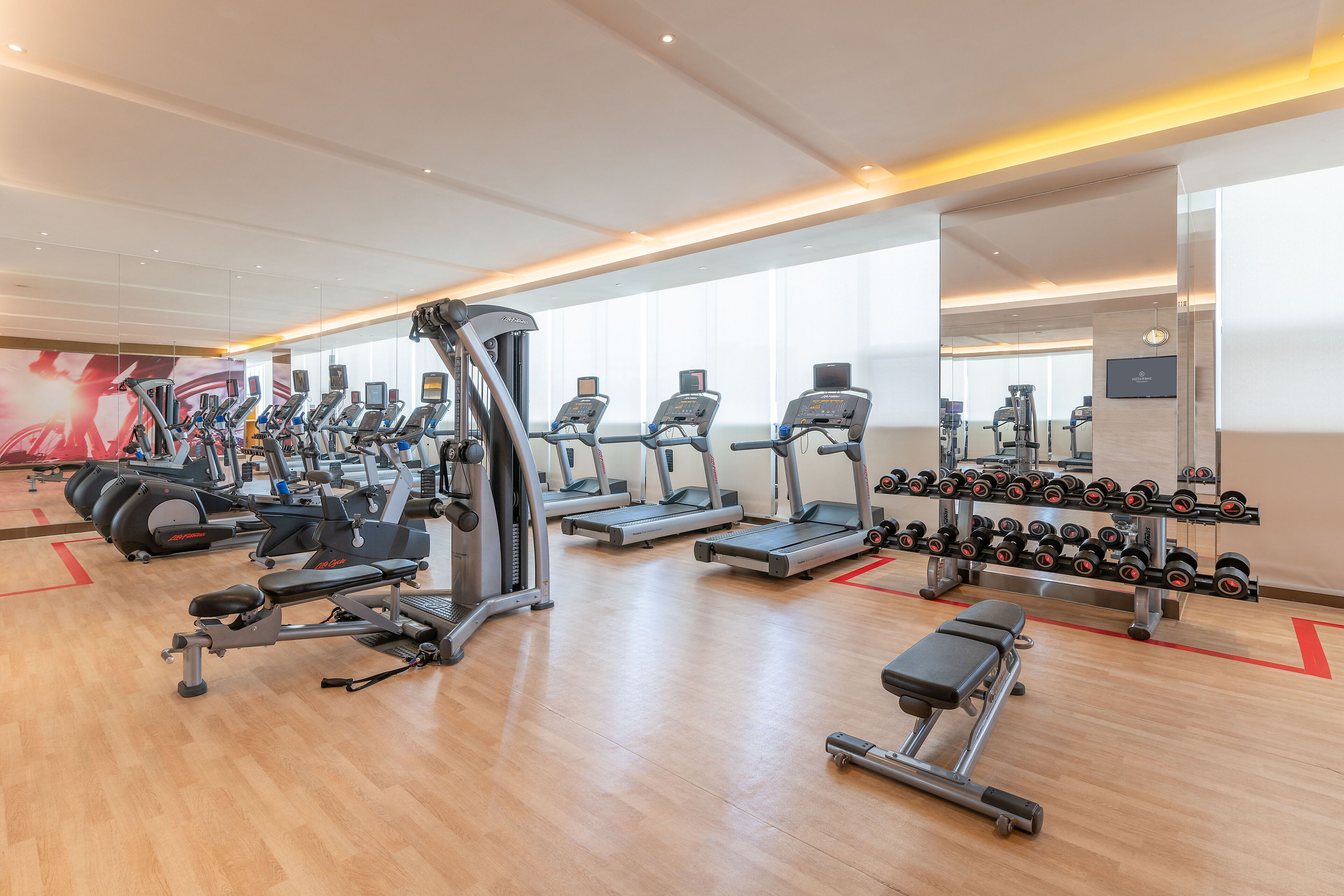 A modern gym with various cardio machines, weightlifting equipment, and a mirror wall.