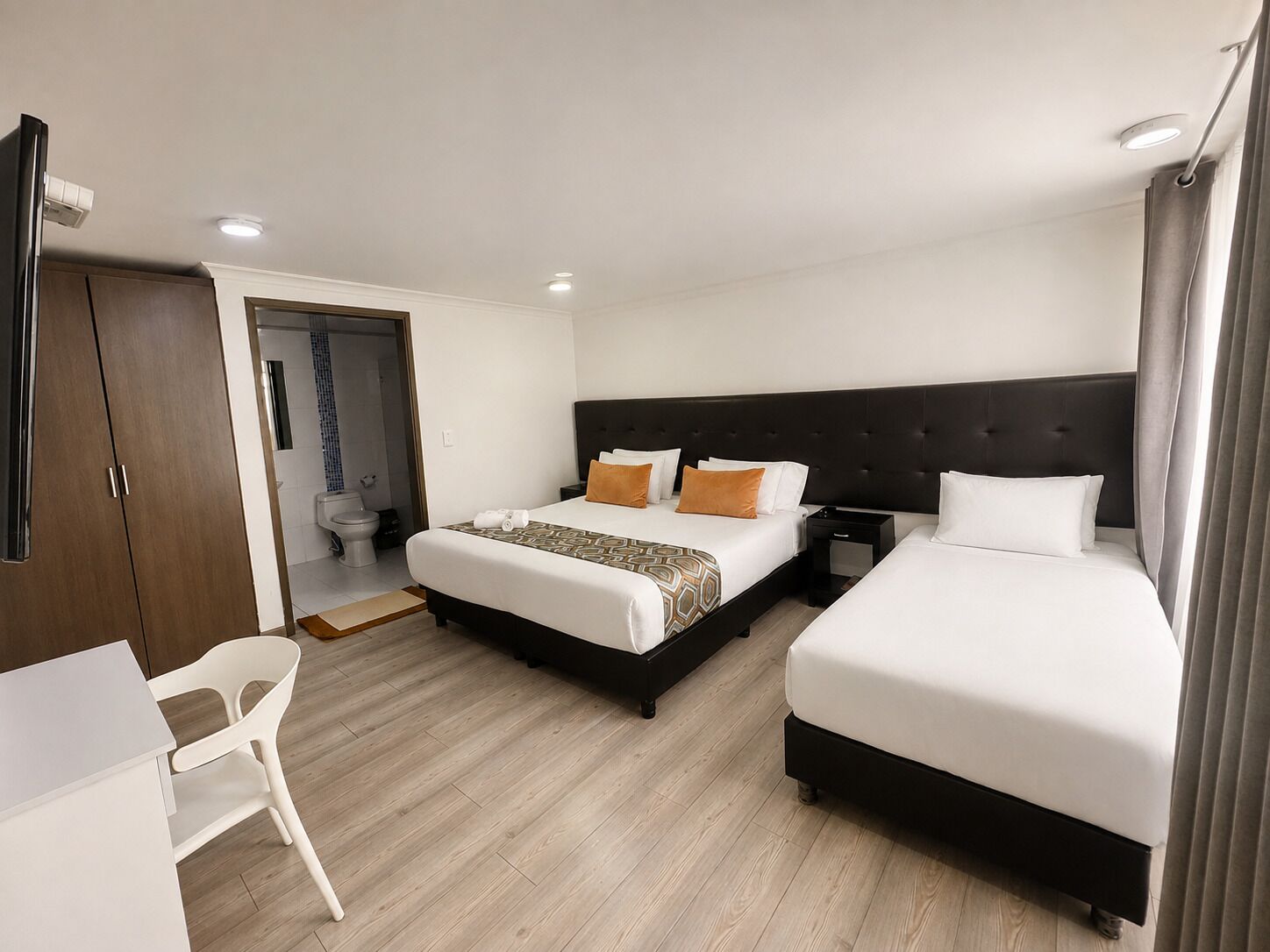 Una habitación de hotel con dos camas, un escritorio, una silla y un armario.