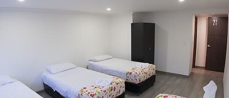 Una habitación de hotel con cuatro camas individuales, un armario y una puerta que da a otra habitación.