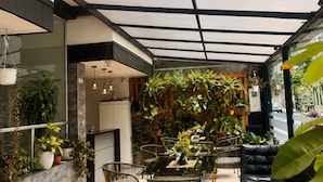 A covered outdoor seating area with tables and chairs, surrounded by potted plants and a stone wall. - Hotel Metro 26 (Bogotá)