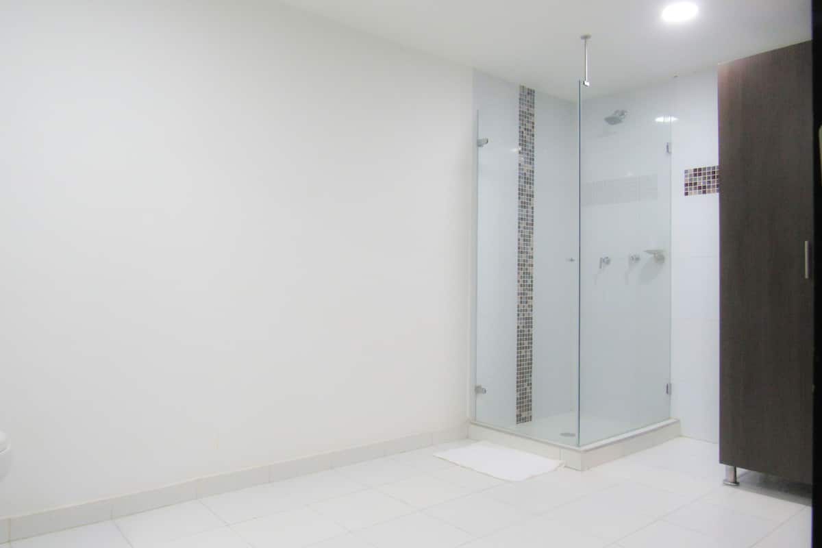 Un baño moderno con baldosas blancas, cabina de ducha de vidrio y mueble de madera oscura.
