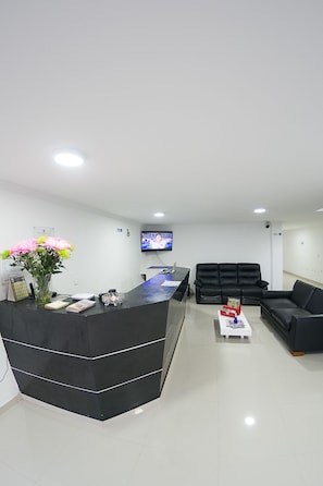 A modern reception area with a black reception desk, a flat-screen TV, and a seating area with black sofas. - Hotel Metro 26 (Bogotá)