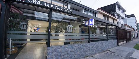 Un hotel con fachada moderna, que presenta un letrero destacado que dice "Metro 26 Hotel" y un letrero azul que indica una oferta.
