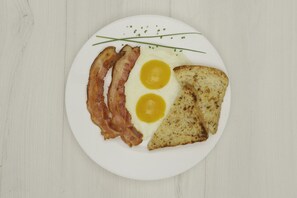 A plate with two fried eggs, two strips of bacon, and two pieces of toast on a white plate. - Hotel Metro 26 (Bogotá)